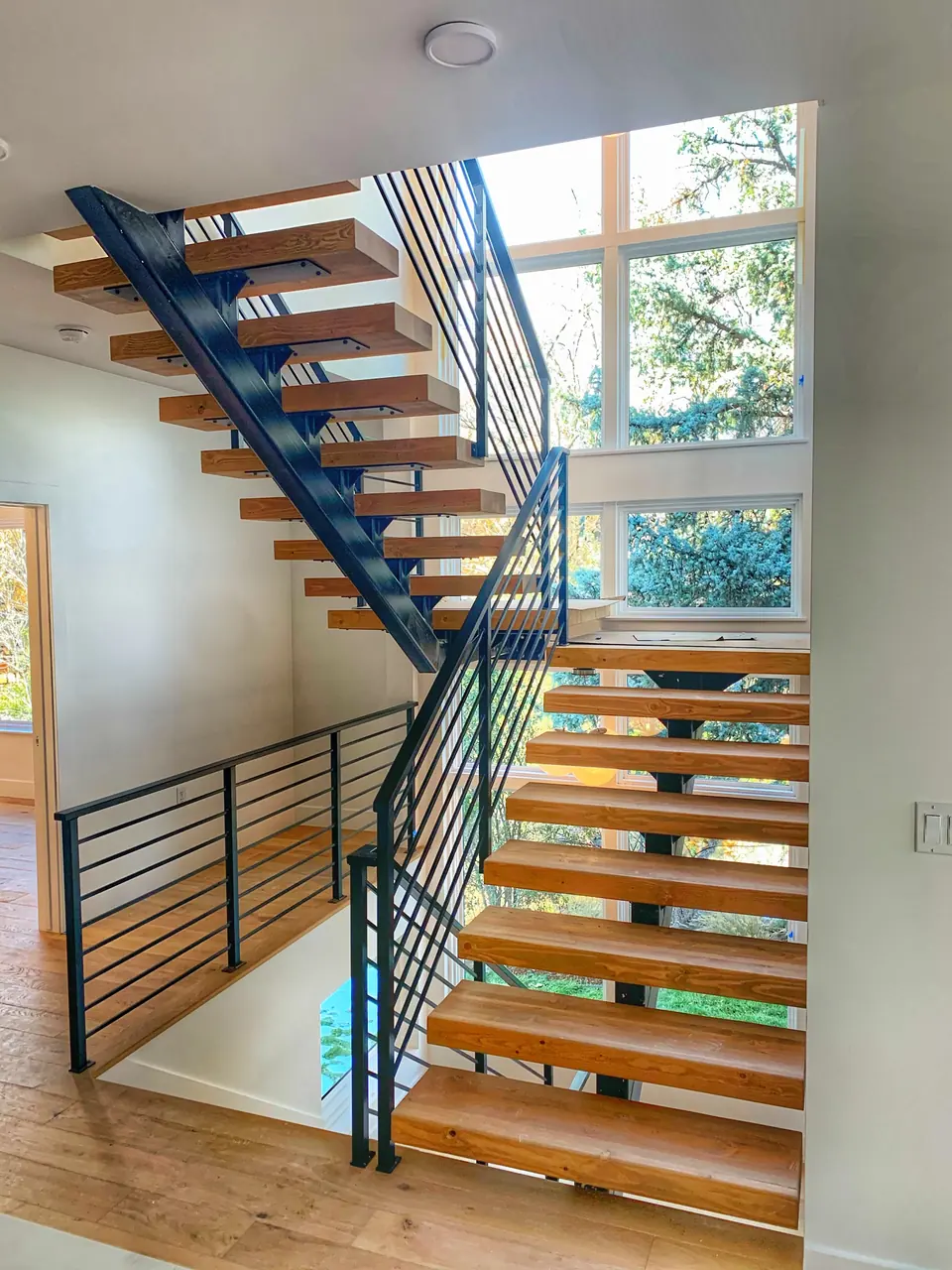 Open-riser stair with a black steel stringer and horizontal bar railing